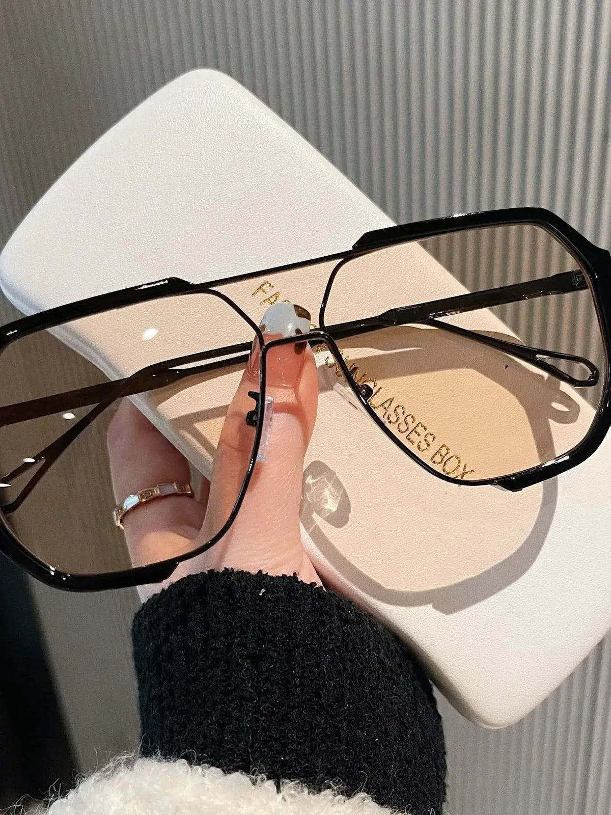 UV Protection Oversized Sunglasses held above a stylish glasses case, showcasing their sleek design and UV400 protection.