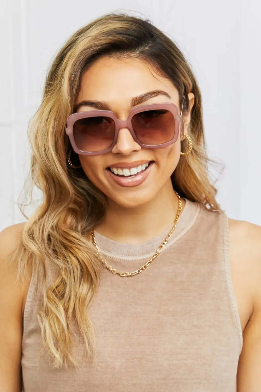 Woman wearing square hybrid sunglasses UV400 with soft pink frame and gradient lenses, smiling outdoors.
